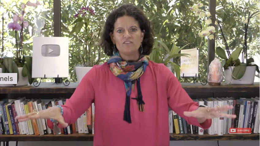 Dr. Mindy Pelz pressents a seminar to an audience. She is standing in front of a book case that is embellished with orchids.