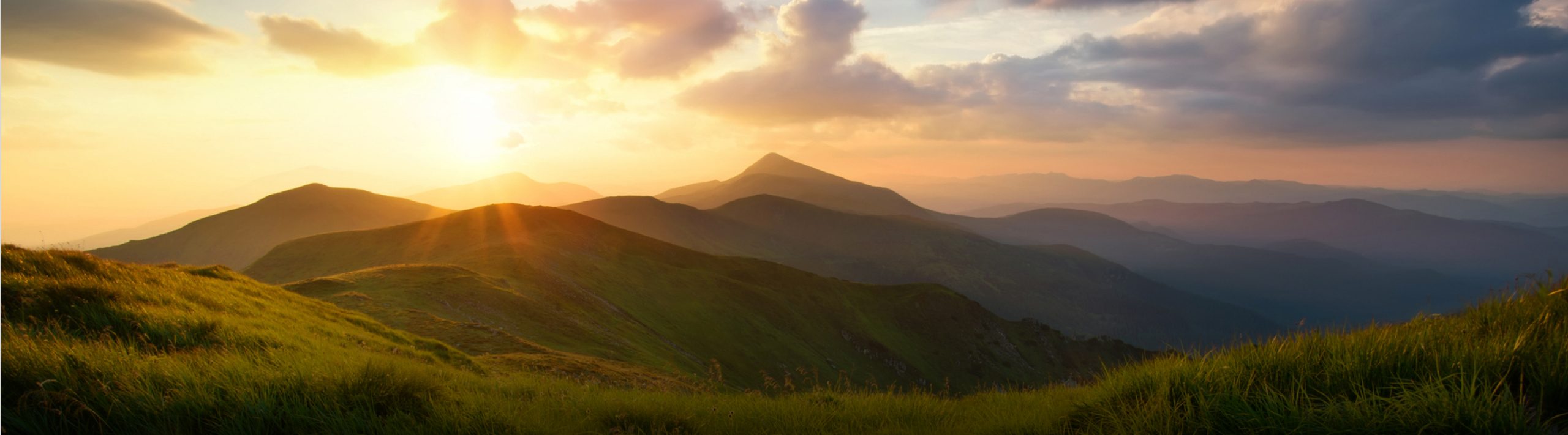 A landscape picture of mountains with the sun rising above the mountains